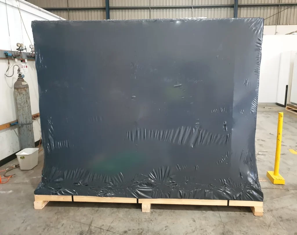 Shrink wrap covering a machine and machine is on top of a wooden machine base