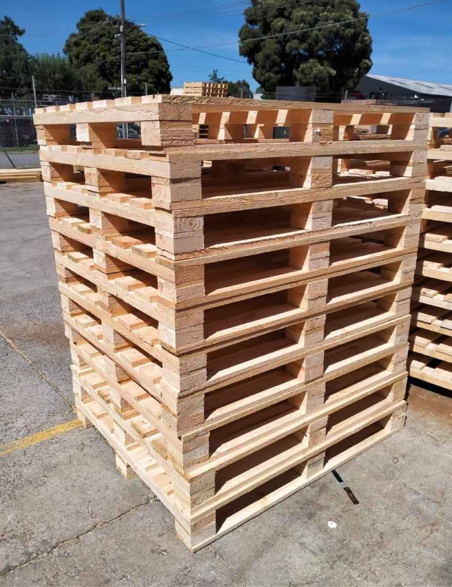 wooden block pallets stacked with plain pallets in background and image of Crate n Pack Solutions logo in background
